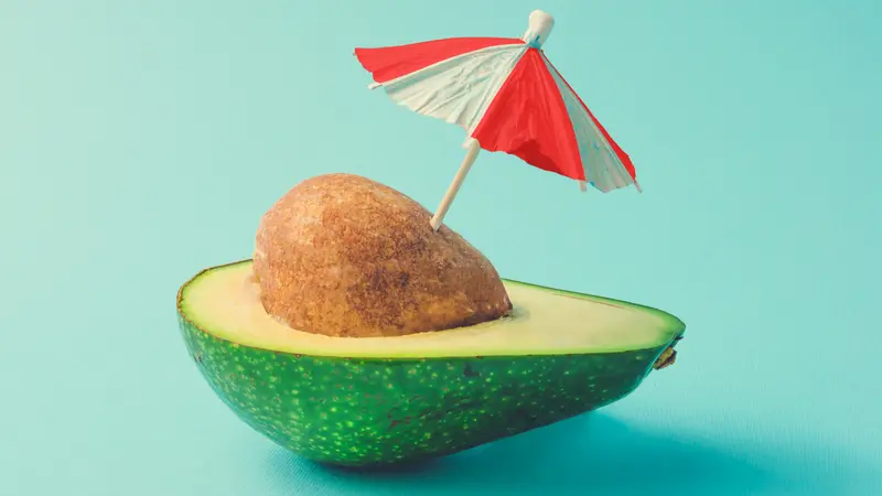 Tropical beach concept made of avocado fruit and sun umbrella.