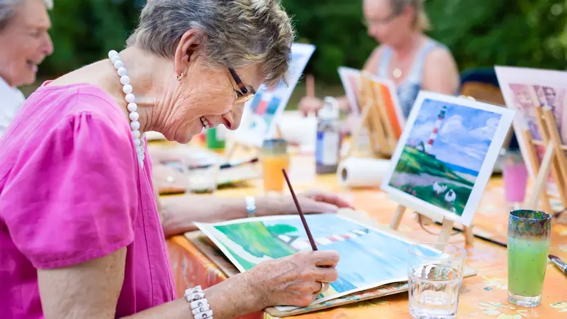 Side view of a happy senior woman smiling while drawing as a recreational activity or therapy outdoors together with the group