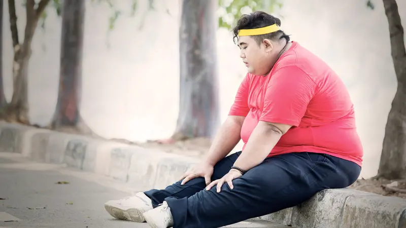 Obese man looks tired after exercising in the park while sitting on the road at autumn time