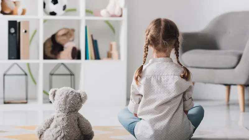 Rear view of little child in white shirt sitting on floor with teddy bear practicing mindfulness Rear view of little child in white shirt sitting on floor with teddy bear practicing mindfulness