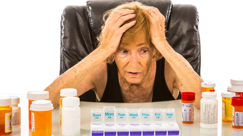 Senior woman overwhelmed with pills to fit in her pill box