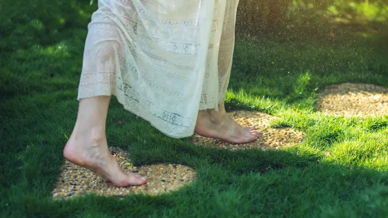 Girl walking barefoot on the stones in heart shape on green grass