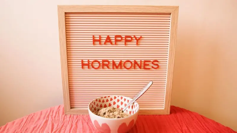 Image of a sign board with the letters Happy Hormones with a bowl of ice cream in front sitting on a table covered in a crinkly pink tablecloth