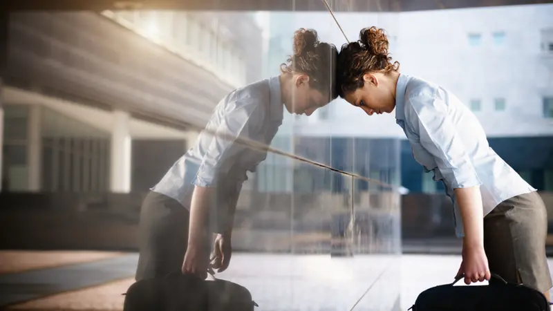 Adult woman banging her head against a wall outside office building.