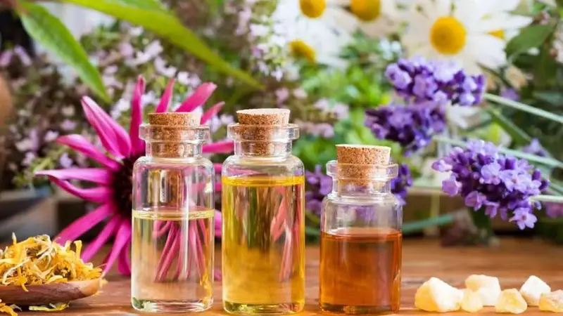 3 glass bottles with cork stoppers filled with liquid sitting on a table filled with flowers and herbs