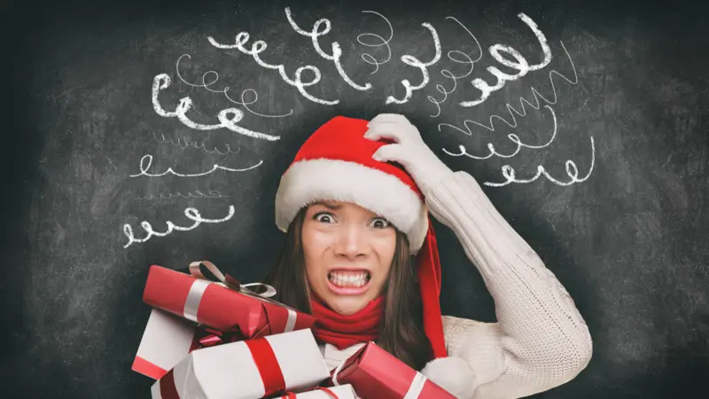 Christmas stress, woman in Santa hat stressed out, drawings of headache spirals on black blackboard 