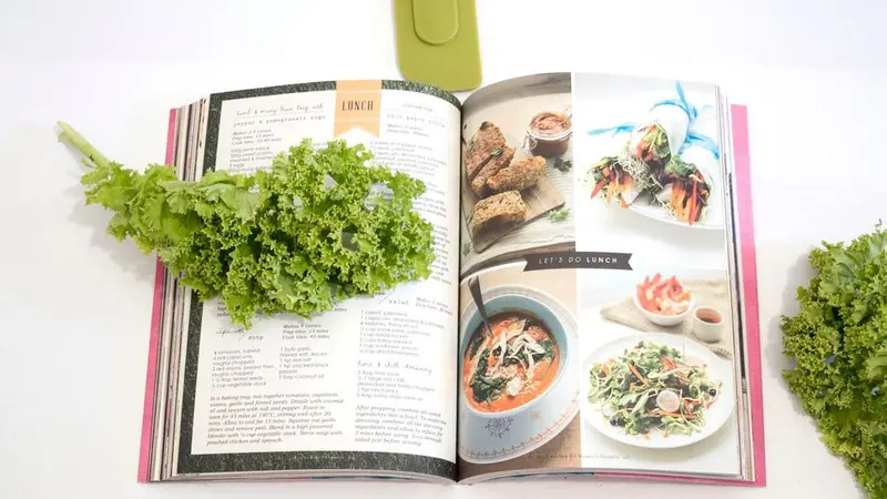 Healthy Gut, Happy Health Recipe Swap Cookbook lying open on white table with a piece of kale draped over the left page