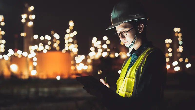 Asian man engineer using digital tablet working late night shift at petroleum oil refinery