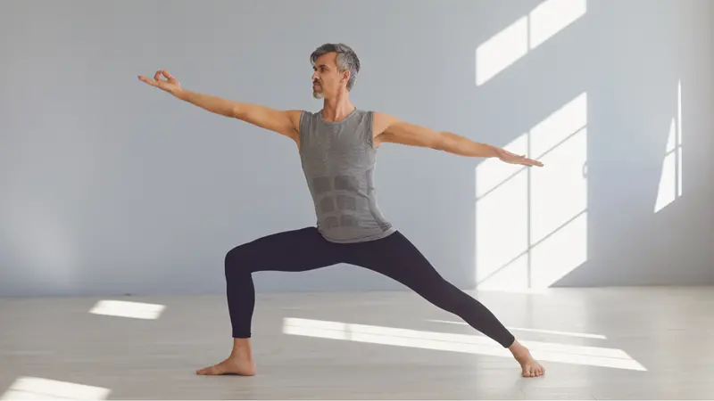 A man is practicing yoga balance in a gray room.