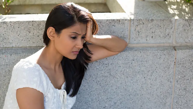 Closeup of young woman in white dress sitting on bench, really depressed, isolated gray background. 