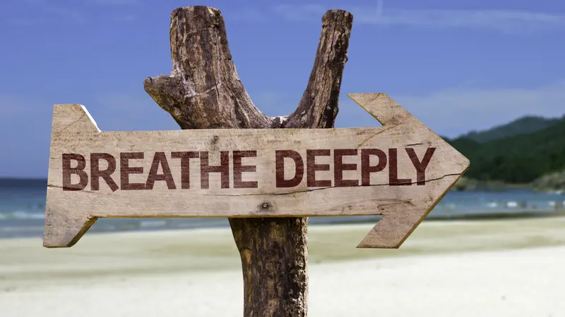 Breathe Deeply wooden sign with a beach on background