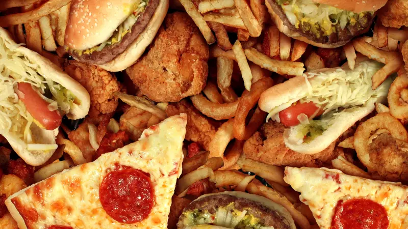 Fast food concept with greasy fried restaurant take out as onion rings burger and hot dogs with fried chicken french fries and pizza as a symbol of diet temptation resulting in unhealthy nutrition