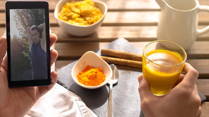 Selective focus of a person having breakfast with golden milk turmeric and Indian cinnamon for energy while looking at the cell phone a guy doing stretching and exercises 