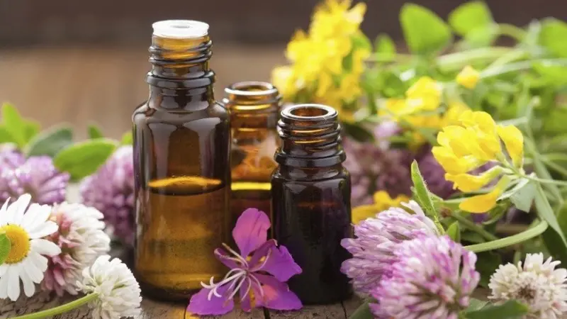 3 amber essential oil bottles sitting on a table surrounded by flowers. 