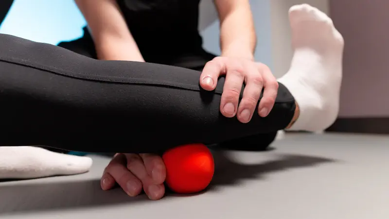 Close-up young male massage therapist teaches a woman myofascial self-massage using a massage ball indoors.