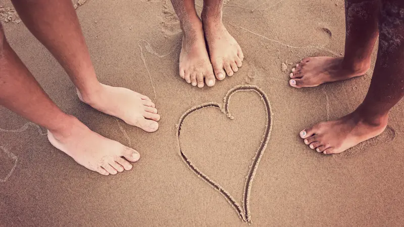 Racially diverse children's feet at the beach with a heart drawn