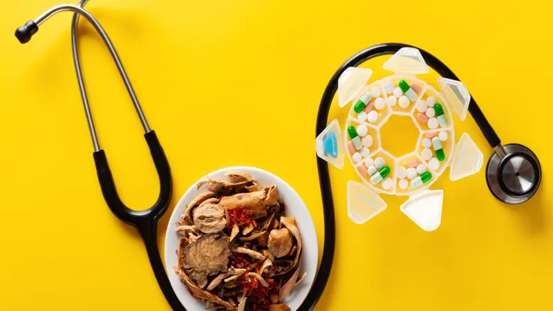 Chinese herb medicine and pills wrapped with a stethoscope on yellow background