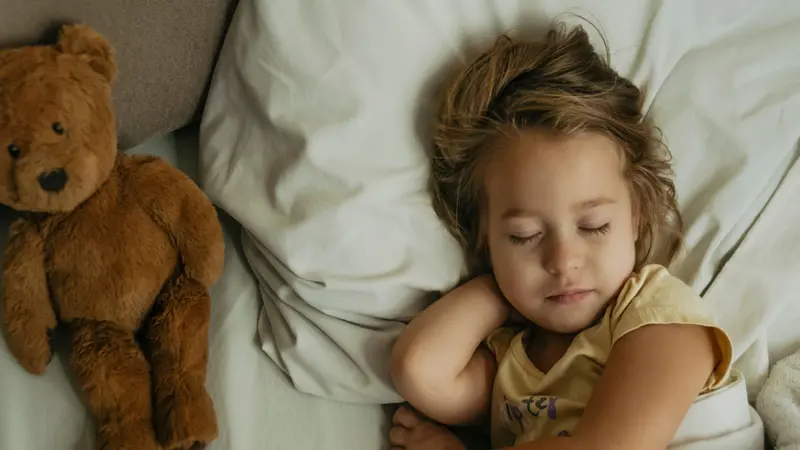 Portrait of cute little girl sleeping in bed with toy bear.