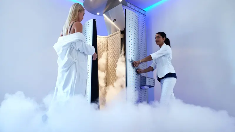 Female taking cryotherapy treatment with beautician standing at the capsule door.