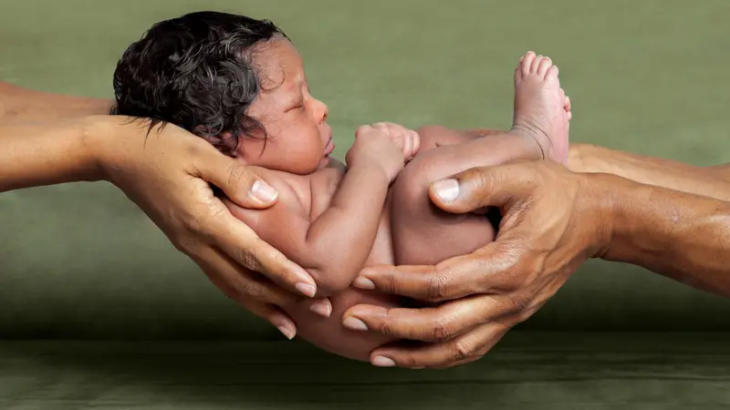 An isolated image of African American parent hands holding their newborn, baby girl in front of a green background. An isolated image of African American parent hands holding their newborn, baby girl in front of a green background.