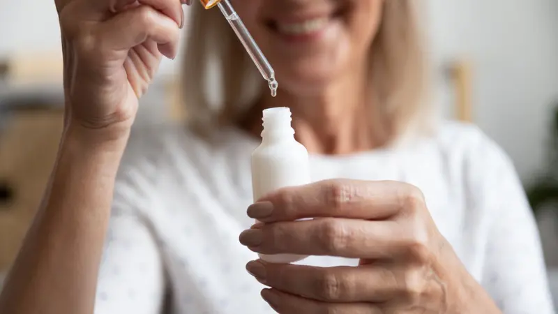 Close up happy older woman opening bottle pipetting skincare product.