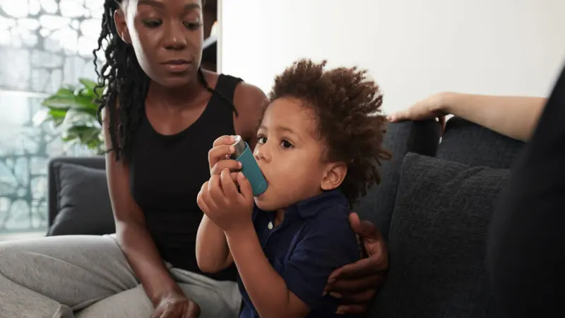 Worried mother looking at son using inhaler when having asthma attack at home Worried mother looking at son using inhaler when having asthma attack at home