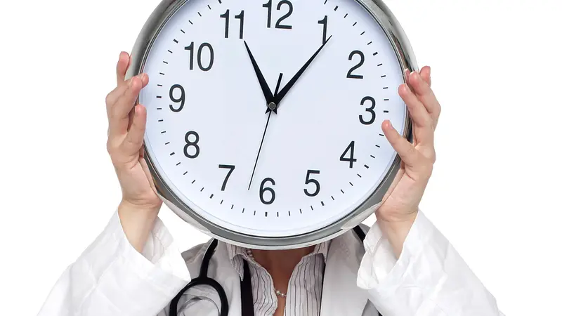 Shot of medical professional holding up wall clock before her face.