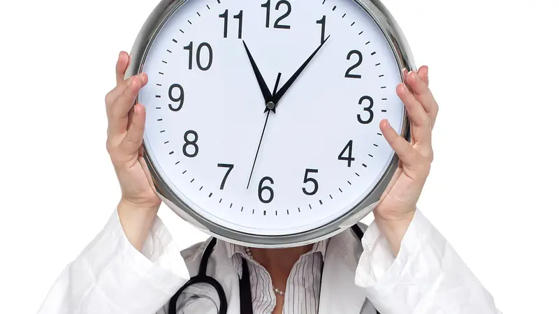 Shot of medical professional holding up wall clock before her face. Shot of medical professional holding up wall clock before her face.