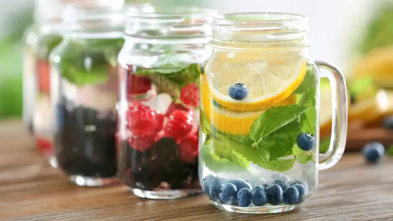 Mason jars of infused water with fruits and berries on wooden table