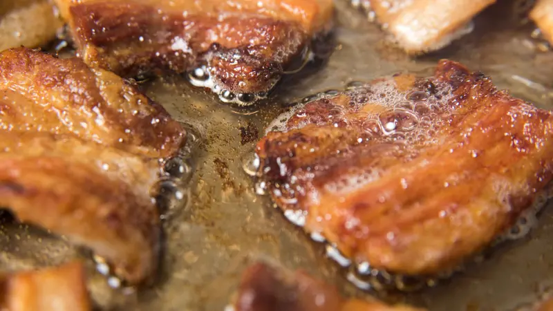 Rendering Fat out of Pieces of Pork Belly in Stainless Steel Skillet Rendering Fat out of Pieces of Pork Belly in Stainless Steel Skillet