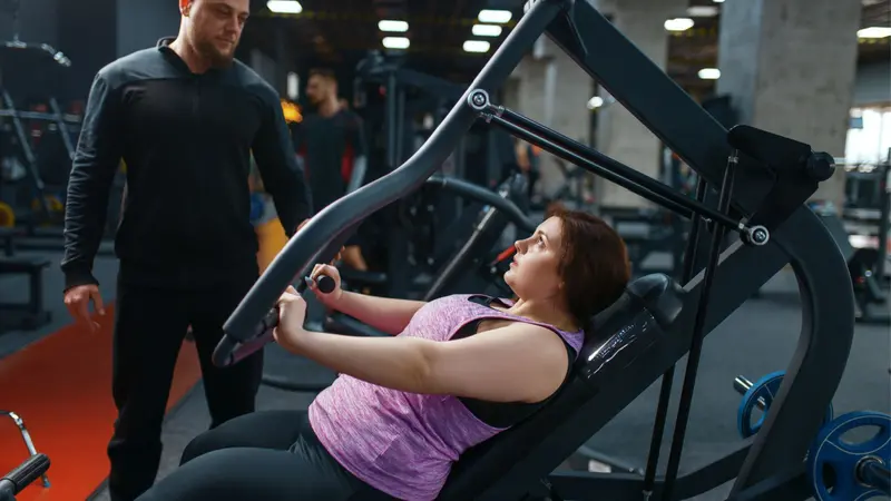 Overweight woman with trainer doing exercise on weight machine Overweight woman with trainer doing exercise on weight machine