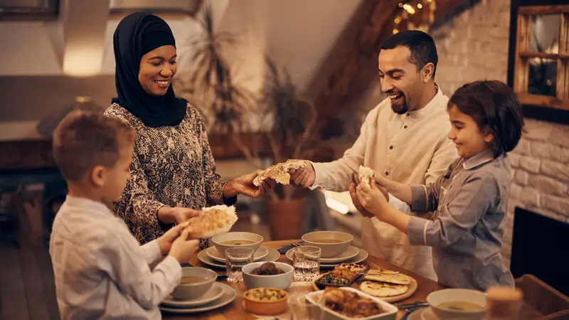 Happy Muslim parents and their kids sharing pita bread while eating dinner Happy Muslim parents and their kids sharing pita bread while eating dinner