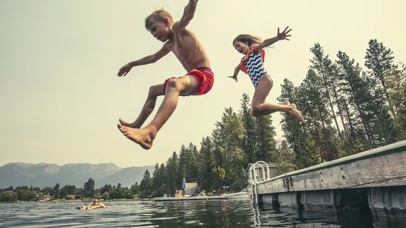 Kids jumping off the dock into a beautiful mountain lake. 