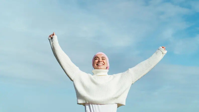 Happy young woman with cancer with arms up. She is wearing a pink scarf on her head and white jersey. Happy young woman with cancer with arms up. She is wearing a pink scarf on her head and white jersey.