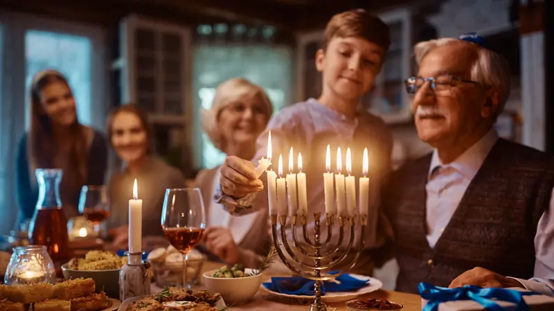 Close up of kid and his extended family lighting the menorah during dinner at dinning table on Hanukkah.