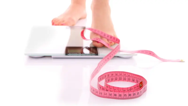 A picture of female feet standing on a bathroom scales and a tape measure over white background