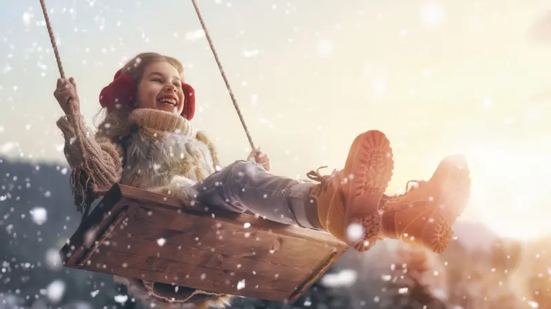 Happy child girl on swing in sunset winter. 