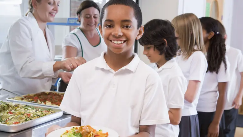 Students in cafeteria line with one holding his healthy meal and looking at camera