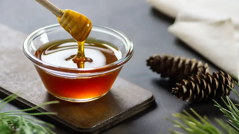 Bowl with honey stick and pine cones on rustic table Bowl with honey stick and pine cones on rustic table