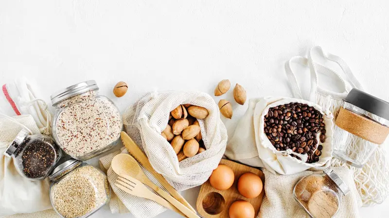 Nuts, dried fruits and groats in eco cotton bags and glass jars on white table in the kitchen. Zero Waste Food Shopping. Waste-free living