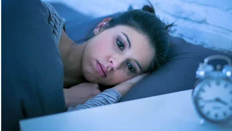 Sad and worried Latin woman unable to sleep at night lying on bed awake