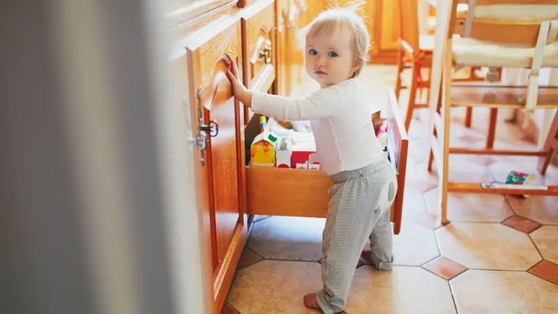 Toddler girl at home, opening the snack drawer in the kitchen and selecting food