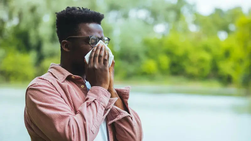 Man with seasonal allergies blowing on wipe in a park on spring day