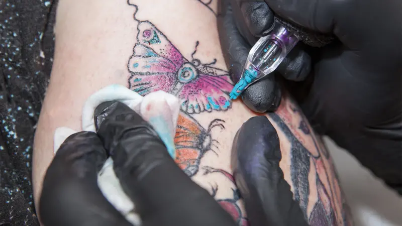 Tattoo artist applies light blue color to a tattoo