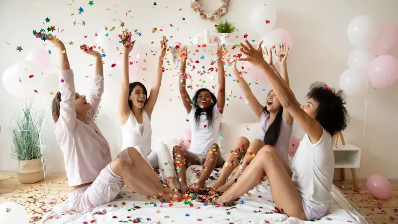 Festive young mixed race female best friends throwing colorful confetti
