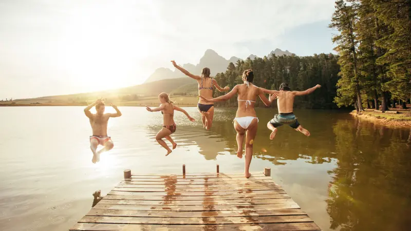 Young friends jumping into the water from a jetty.