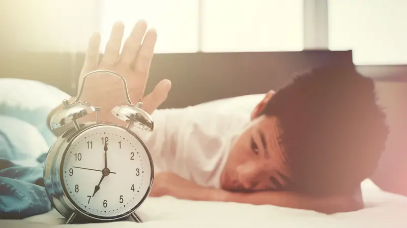 Alarm clock and sleepy teenage boy with hand reaching out for alarm clock Alarm clock and sleepy teenage boy with hand reaching out for alarm clock
