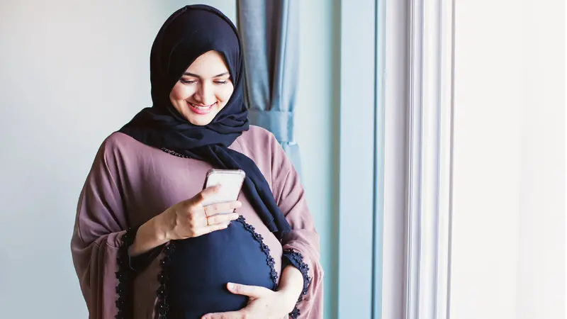 Young pregnant arab woman in hijab using her mobile phone