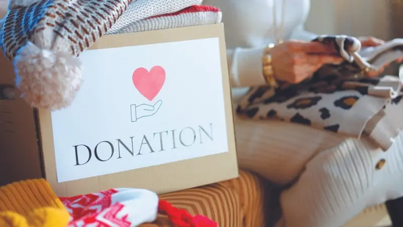 Closeup on donation box and woman packing old warm clothes