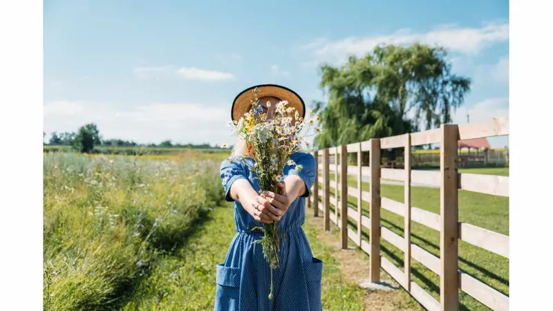 A woman in rustic dress with wildflowers on front of straw bales.